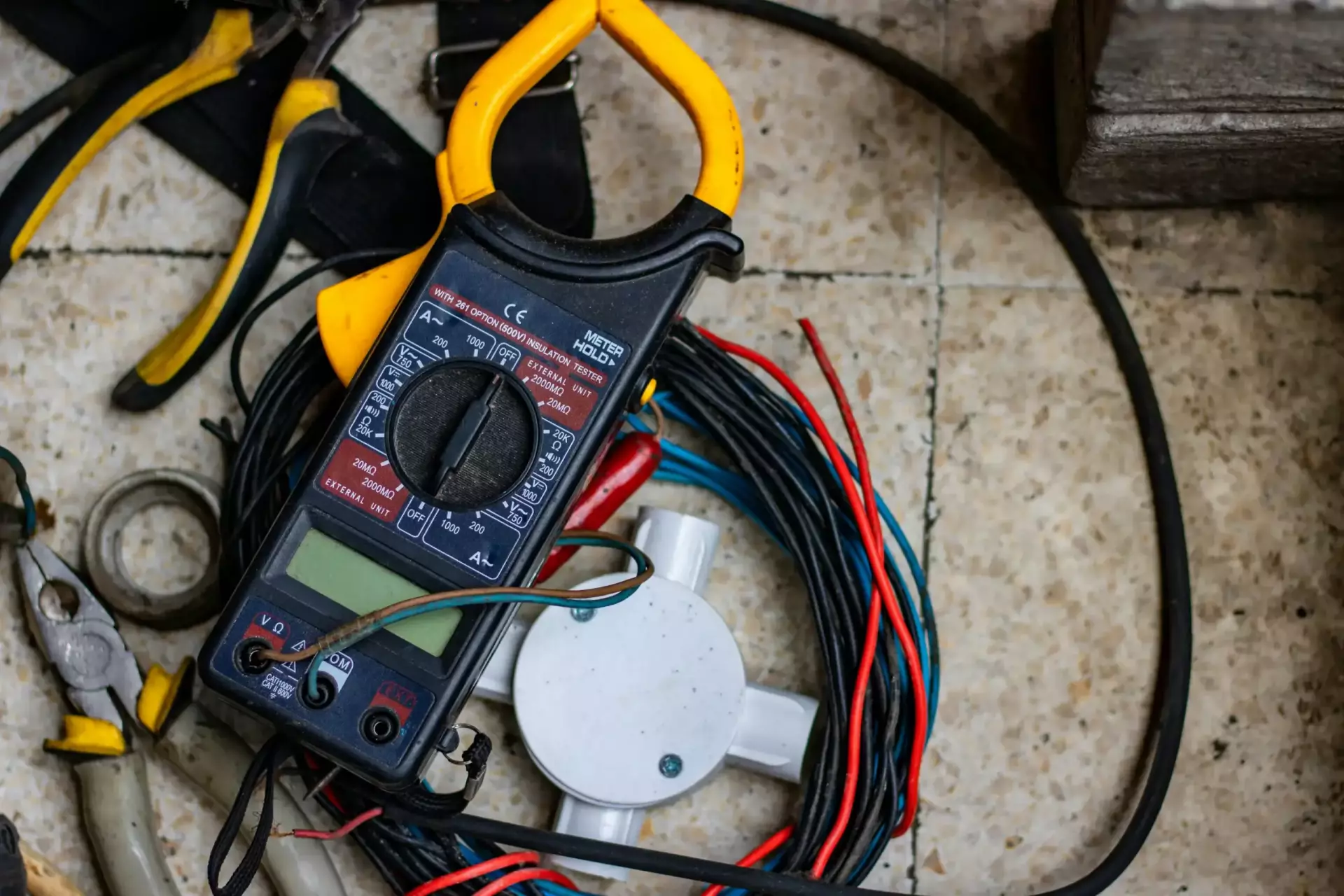 hobi-industri-NLBJ2I0lNr4-unsplash Multimeter und Kabel auf Fliesenboden, umgeben von Werkzeugen für elektrische Reparaturen.