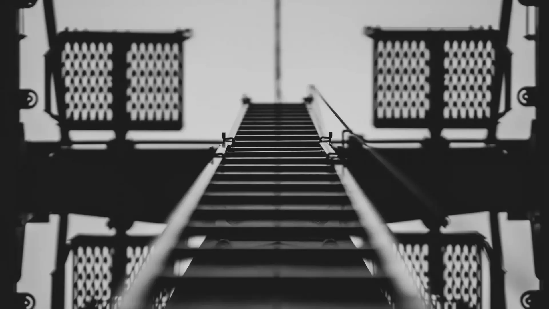 nicolas-krebs-B_1zYZ0cM_E-unsplash Schwarz-Weiß-Aufnahme einer Metalltreppe, die nach oben führt, umgeben von Industrieelementen.