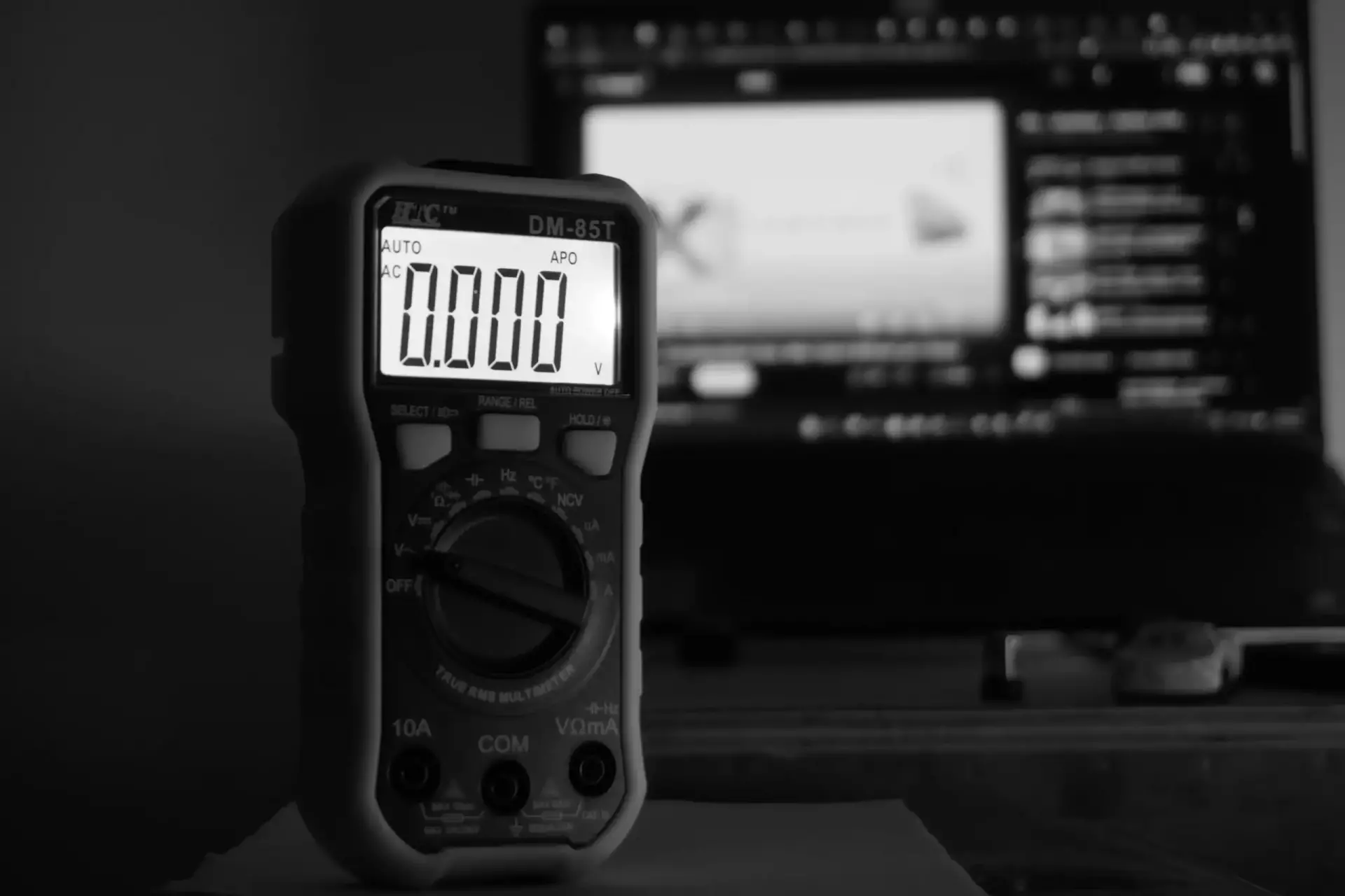 thorium-5g_8GPxWj1Y-unsplash Digitales Multimeter mit Anzeige 0.000 Volt, unscharfer Hintergrund mit Computerbildschirm.